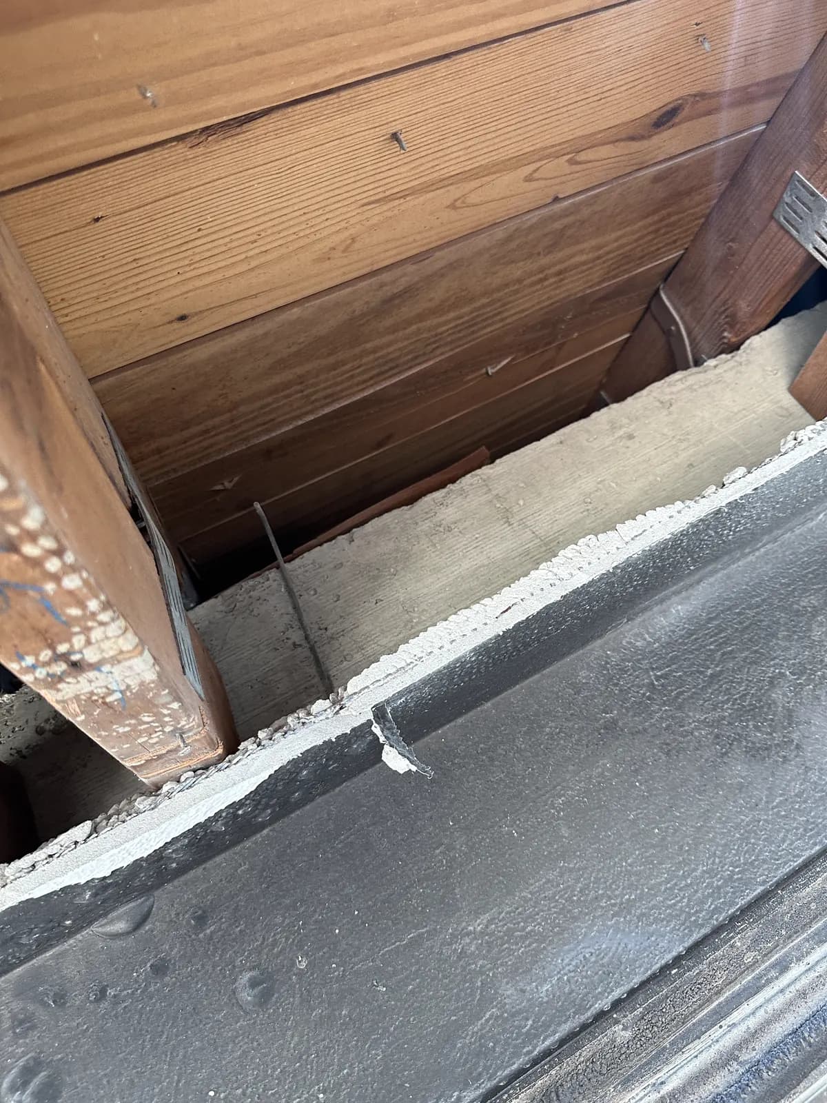 Looking up through a fire-damaged soffit opening at exposed rafters and roof decking above a soot-blackened fascia