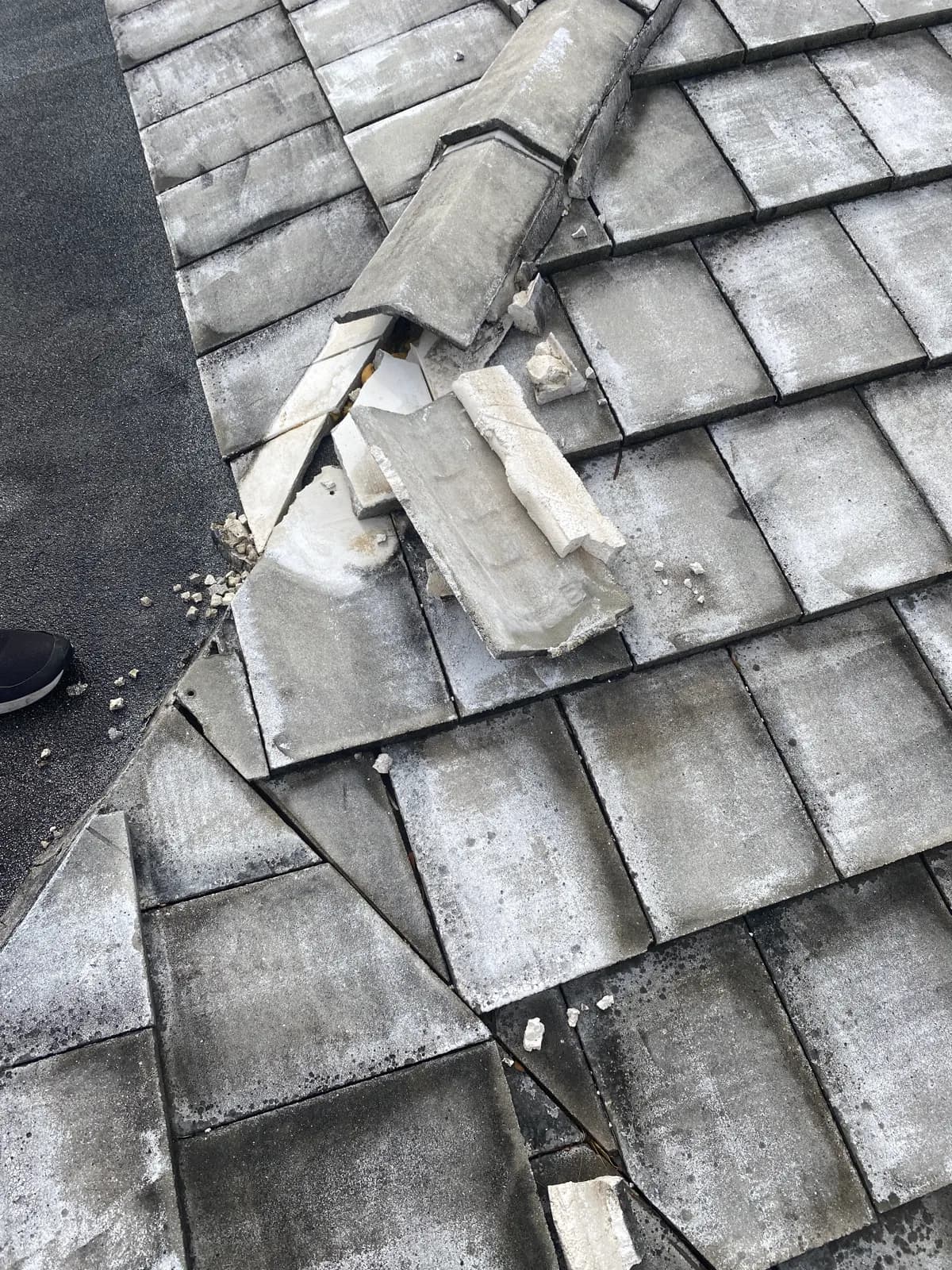 Shattered and displaced hip cap tiles with broken pieces scattered across a flat concrete tile roof slope