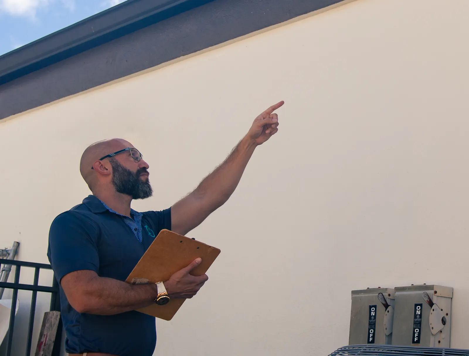 Joe Ford of Dolphin Claims holding a clipboard and pointing up at an exterior wall during a property inspection